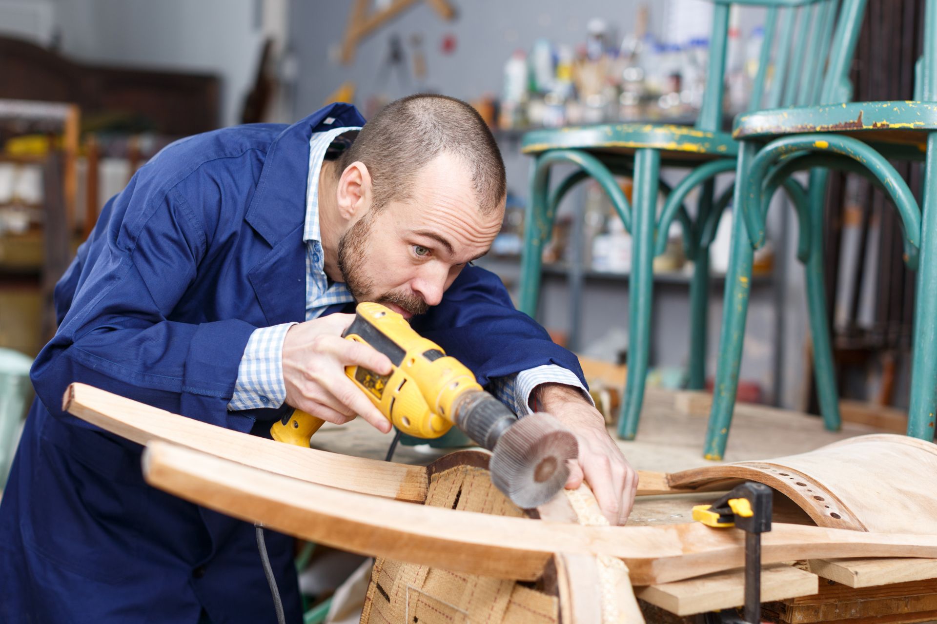 A man is focused on crafting a wooden chair, using tools and materials in a well-lit workshop.