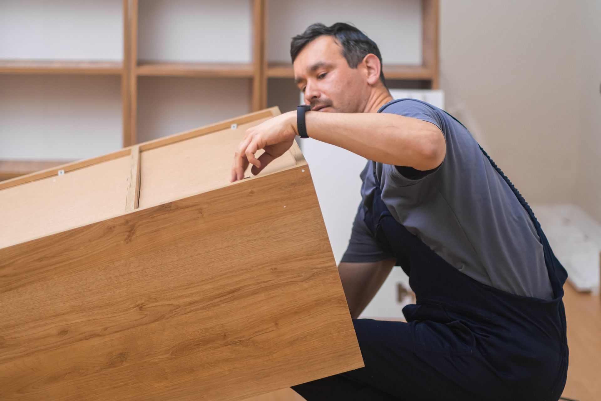 A person is assembling a wooden drawer, focused on aligning its components in a well-lit interior space.