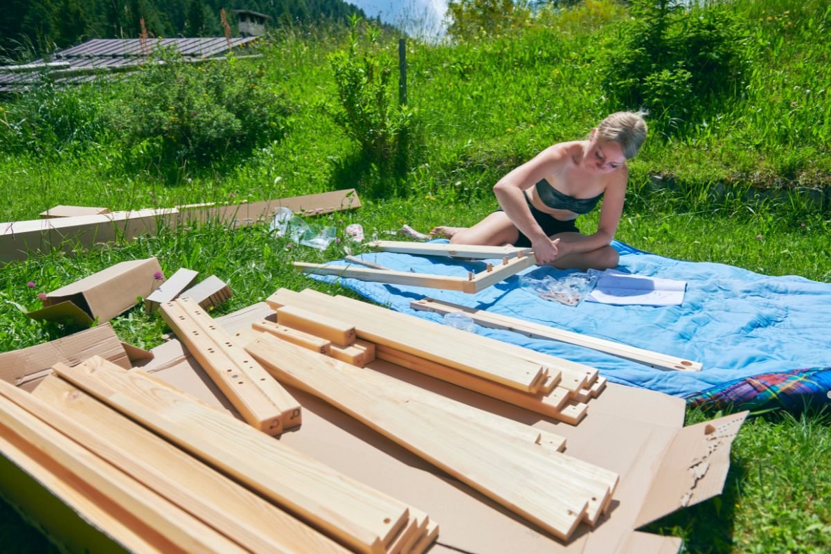 A woman constructs a wooden frame on the grass, showcasing her skills in furniture service.
